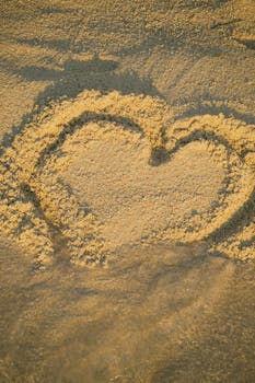Heart shape drawn in sand during golden hour at a tranquil beach in Ksamil, Albania, creating a romantic atmosphere.