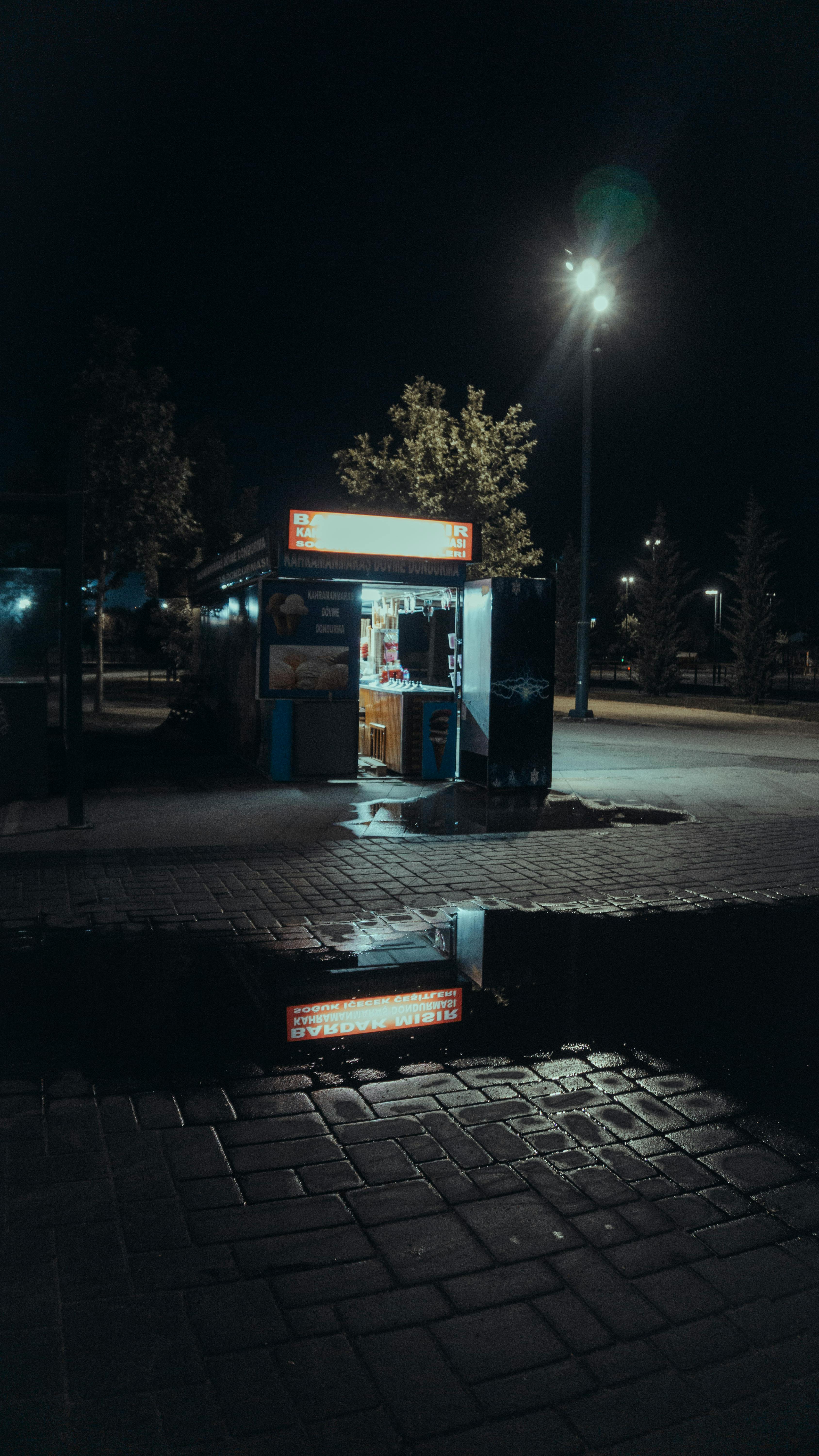 gratis Sfeervol nachtelijk straatbeeld met een verlichte kiosk en zijn weerspiegeling. Stockfoto