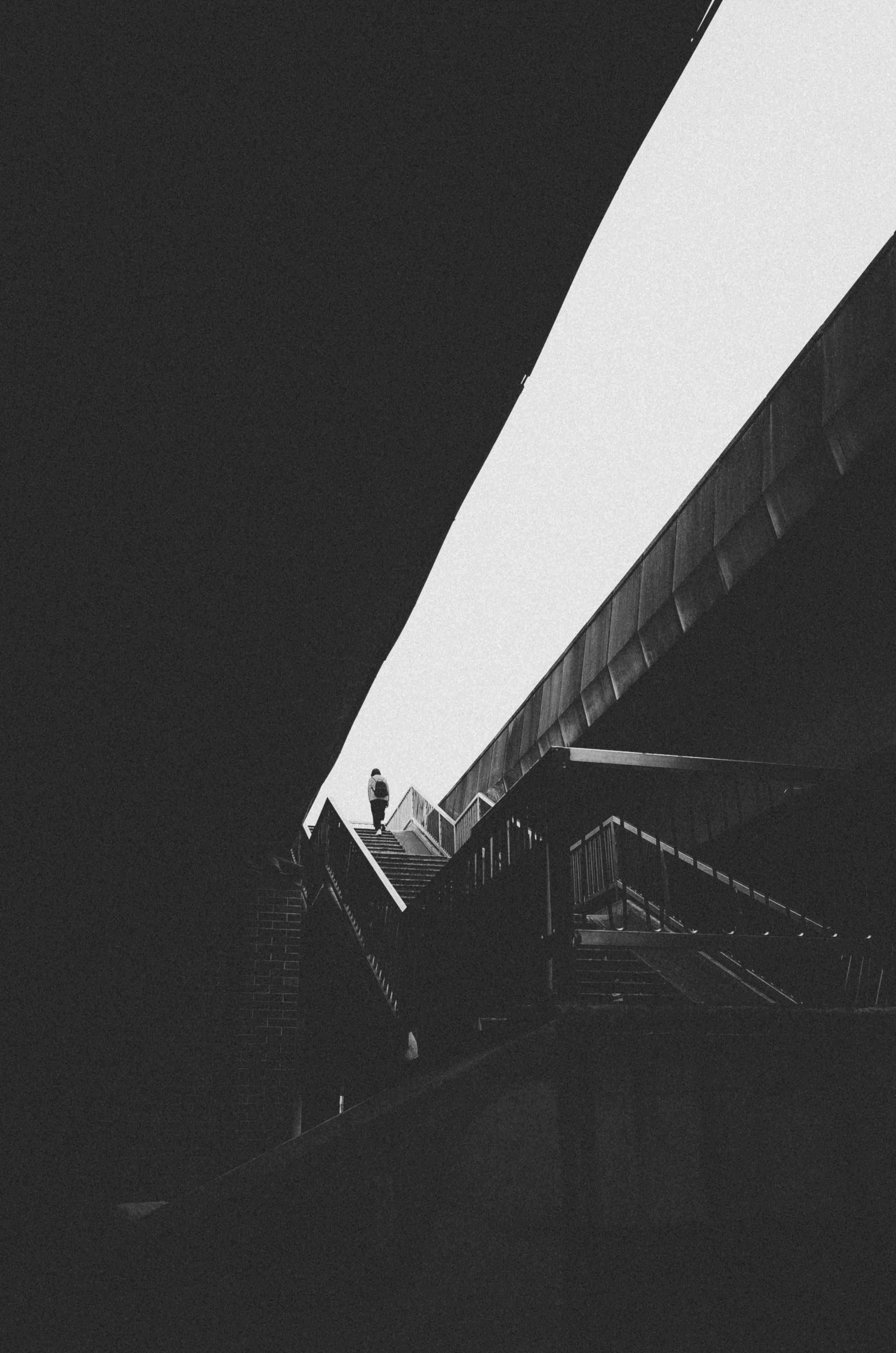 Free Moody black and white photo of a lone figure ascending stairs in an urban setting. Stock Photo