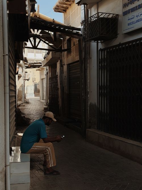 Free Man in urban alleyway using smartphone, enjoying sunlight. City scene. Stock Photo