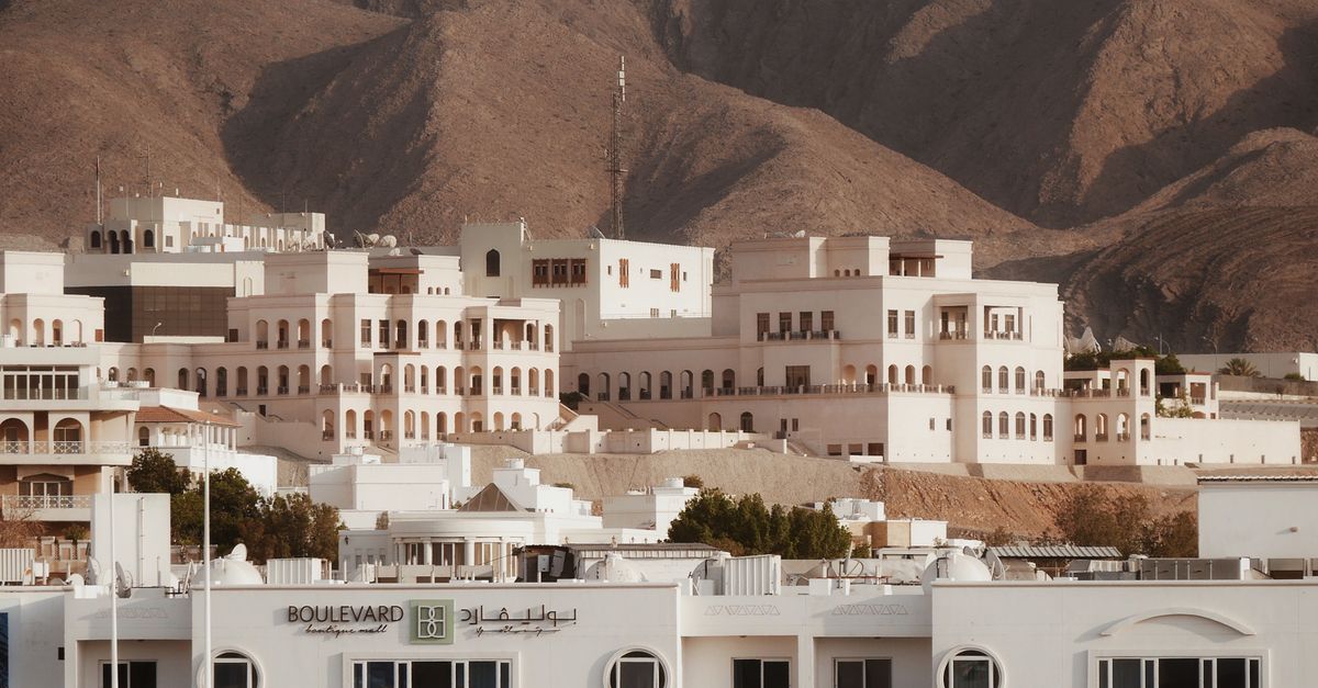 Scenic view of Muscat's traditional architecture against rugged mountains during the day.