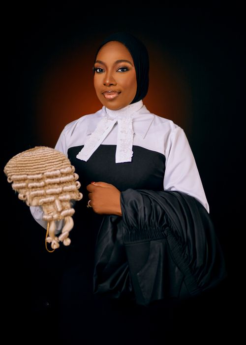 Free Portrait of a poised female lawyer in courtroom attire holding a barrister wig against a dark backdrop. Stock Photo