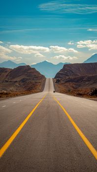 Empty desert highway stretching toward distant mountain range under clear blue sky.