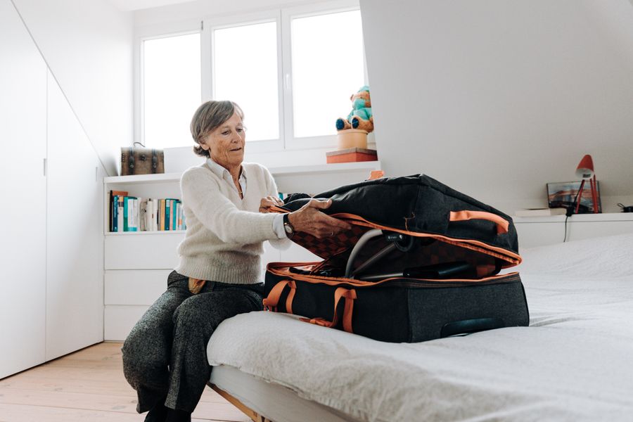 Elderly woman sits on bed packing a suitcase in a bright and modern bedroom