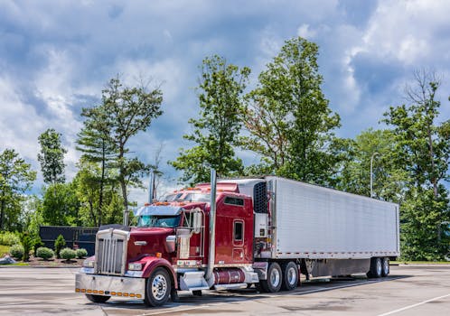 A striking red semi truck parked in a lush scenic area, showcasing modern transportation technology.