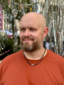 Bald man with a beard and glitter on face, smiling at an outdoor event.