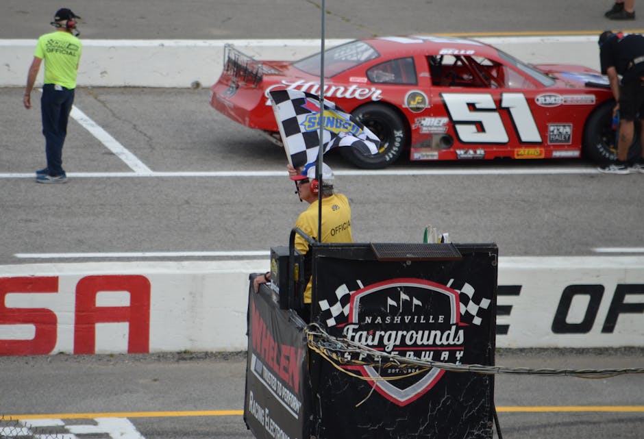 Checker flag waves at Nashville Fairgrounds Speedway during a thrilling car race event.