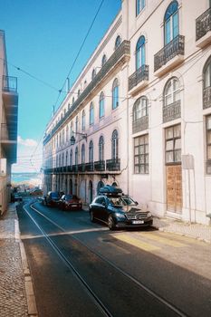 Elegant European architecture on a sunny Lisbon street with parked cars.