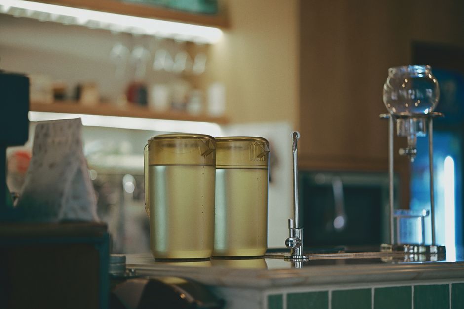 A cozy coffee shop interior featuring brewing equipment and two jugs of water on the counter.