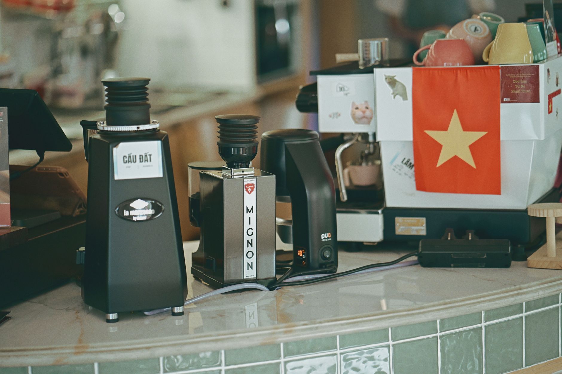 Coffee grinders and espresso machine on a cafe counter, featuring Vietnam flag.