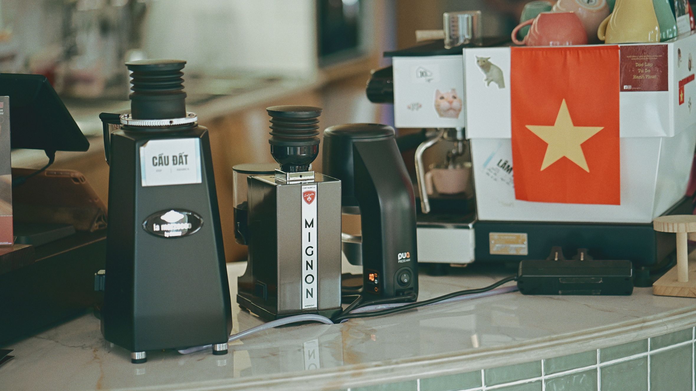 Coffee grinders and espresso machine on a cafe counter, featuring Vietnam flag.