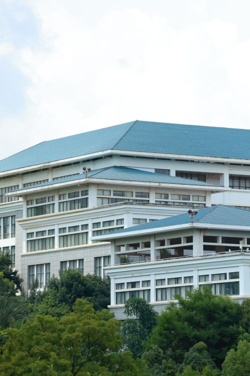 Free Contemporary white building with a blue roof surrounded by lush greenery, captured in daylight. Stock Photo