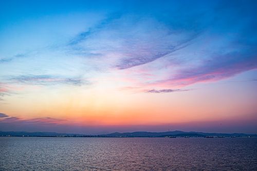 Free Stunning view of a colorful sunset over the ocean with city lights in the distance. Perfect for travel and nature enthusiasts. Stock Photo