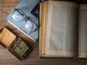 复古布景中，木桌上摆放着古董书籍、手表和阅读眼镜