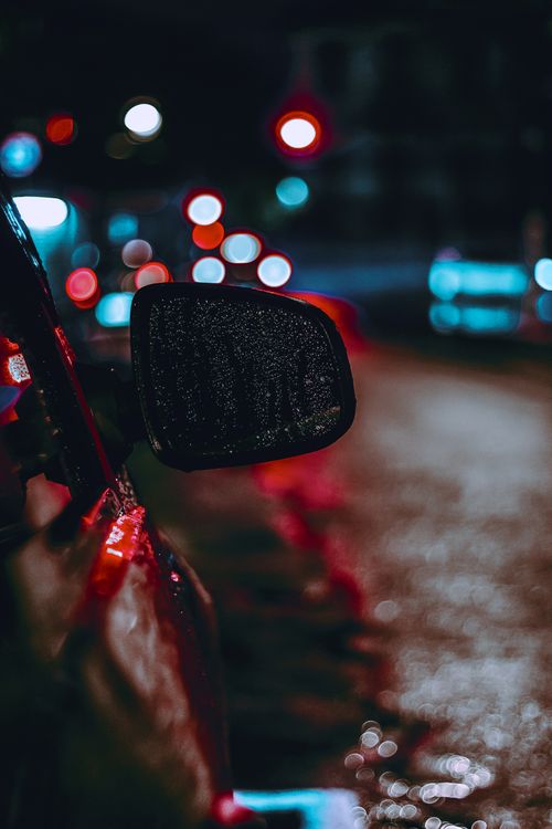 Free Moody street view of a car's side mirror with bokeh lights and rain droplets, highlighting urban night life. Stock Photo