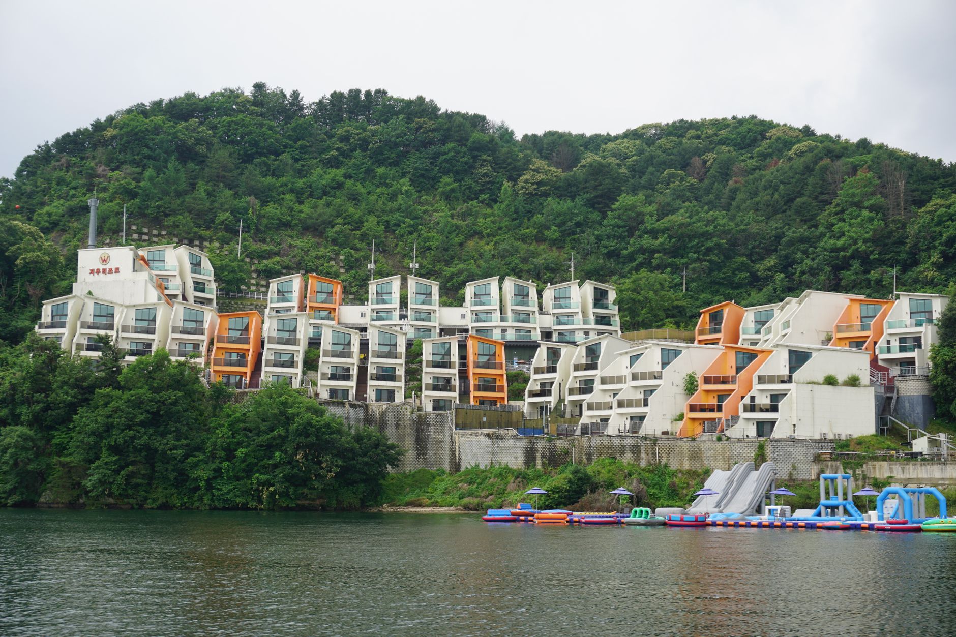 Colorful apartments by a scenic lake with lush green hills in the background.