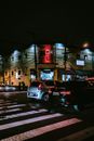 夜晚的城市街道上，汽车行驶在霓虹灯牌和路灯照亮的人行横道上