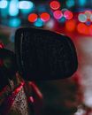 Sidelight of red car in water drops against unrecognizable places with different color lights on street at night