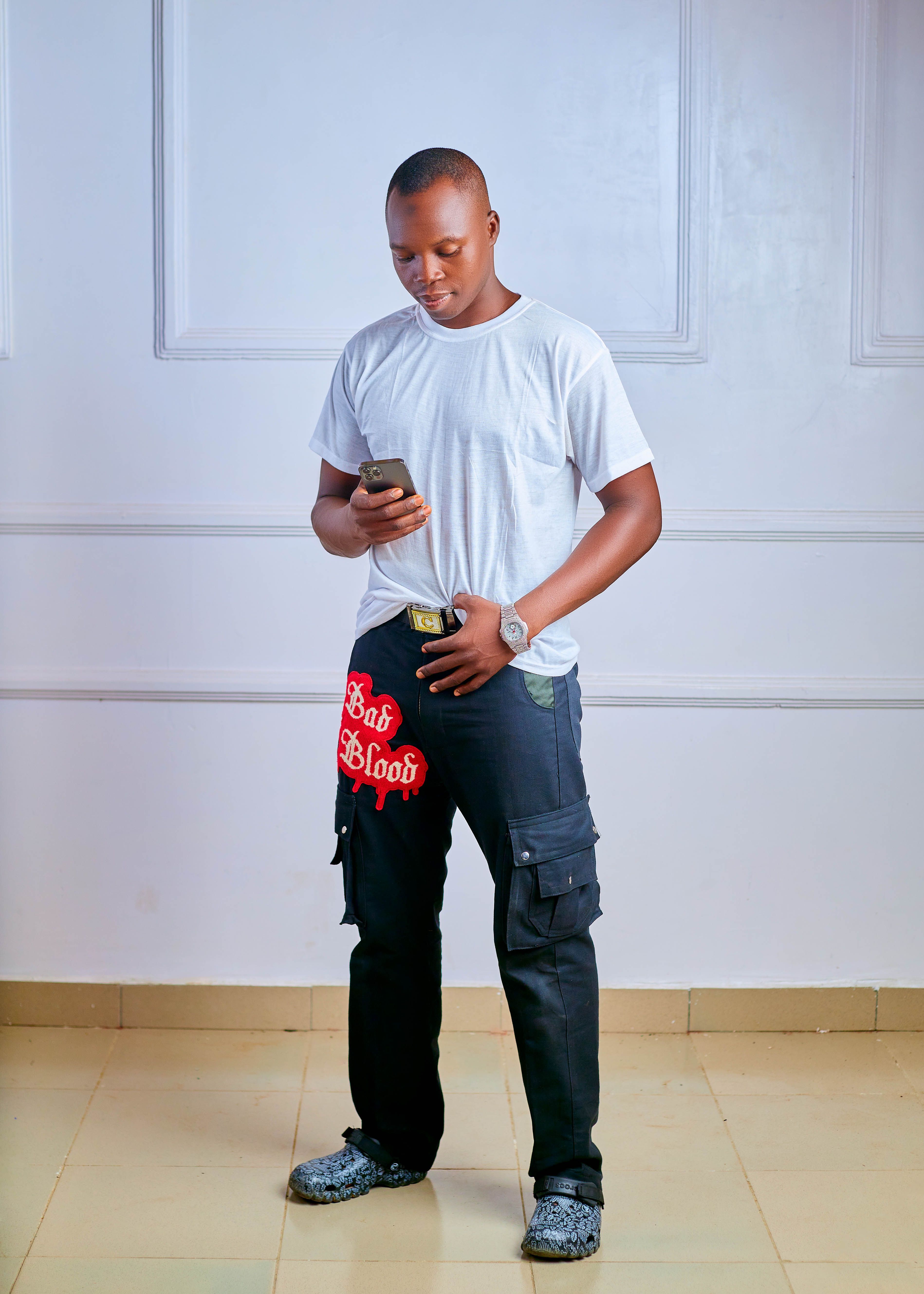 A young adult male wearing casual clothing, checking his phone indoors.