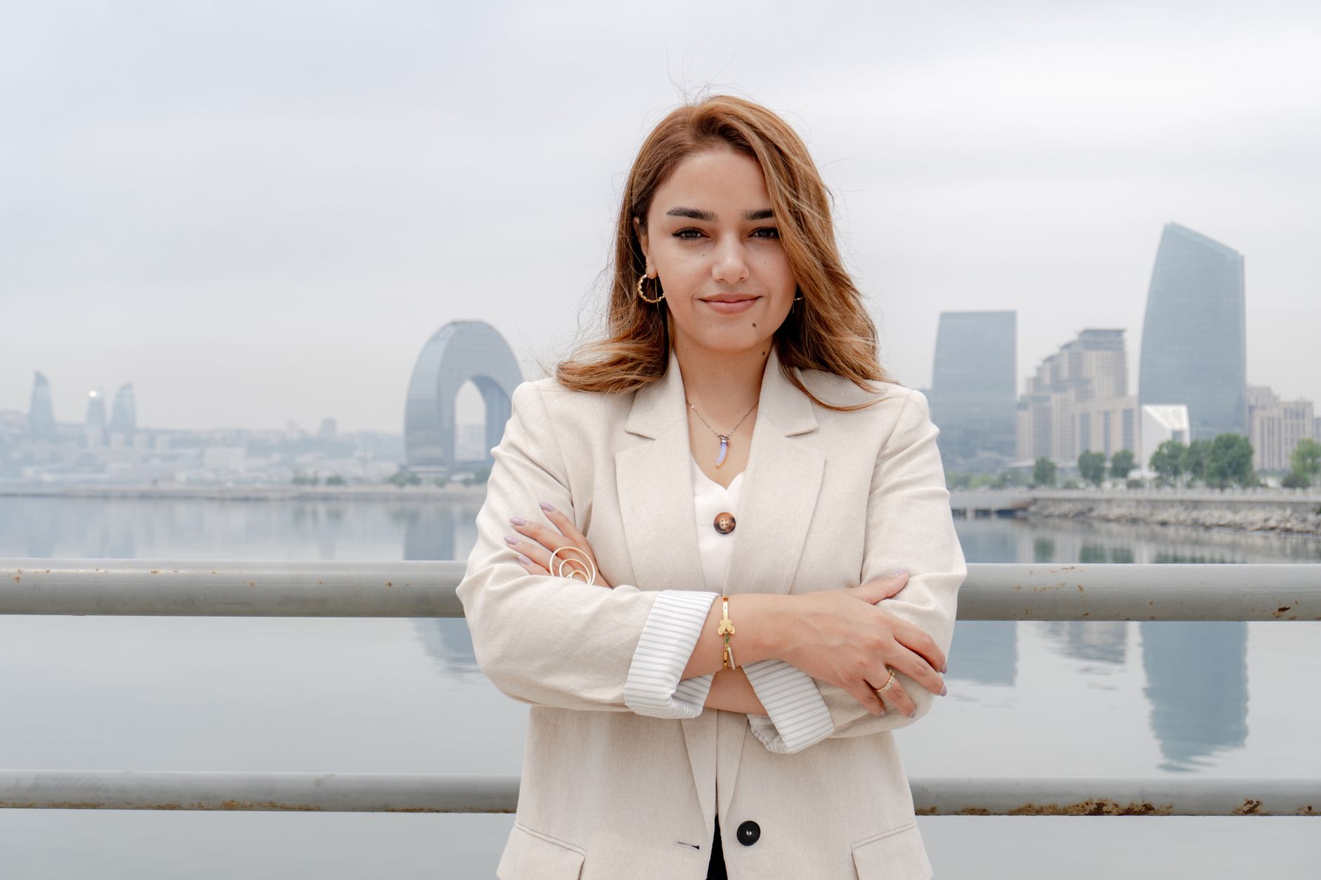 Professional woman in white blazer standing confidently by a waterfront with city skyline in the background. Ideal for business and lifestyle themes.