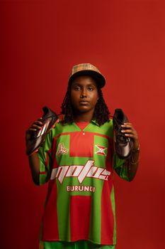 Portrait of a young athlete holding soccer cleats in a colorful sports jersey, indoors.