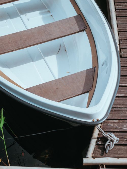 Free A white rowboat moored at a wooden pier on a calm day, showcasing serene waterside scene. Stock Photo