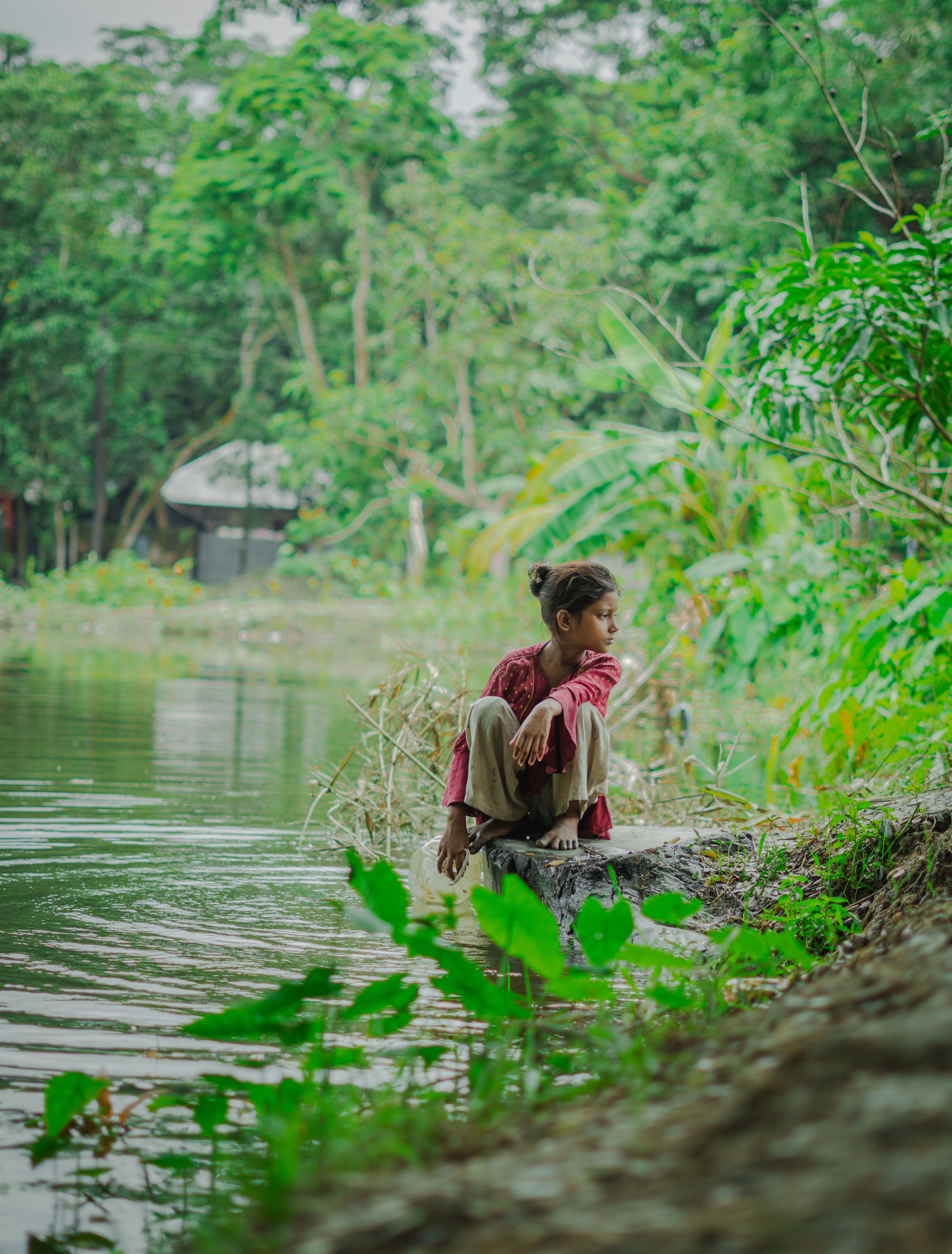 Young Girl Sitting by Tranquil Riverside · Free Stock Photo