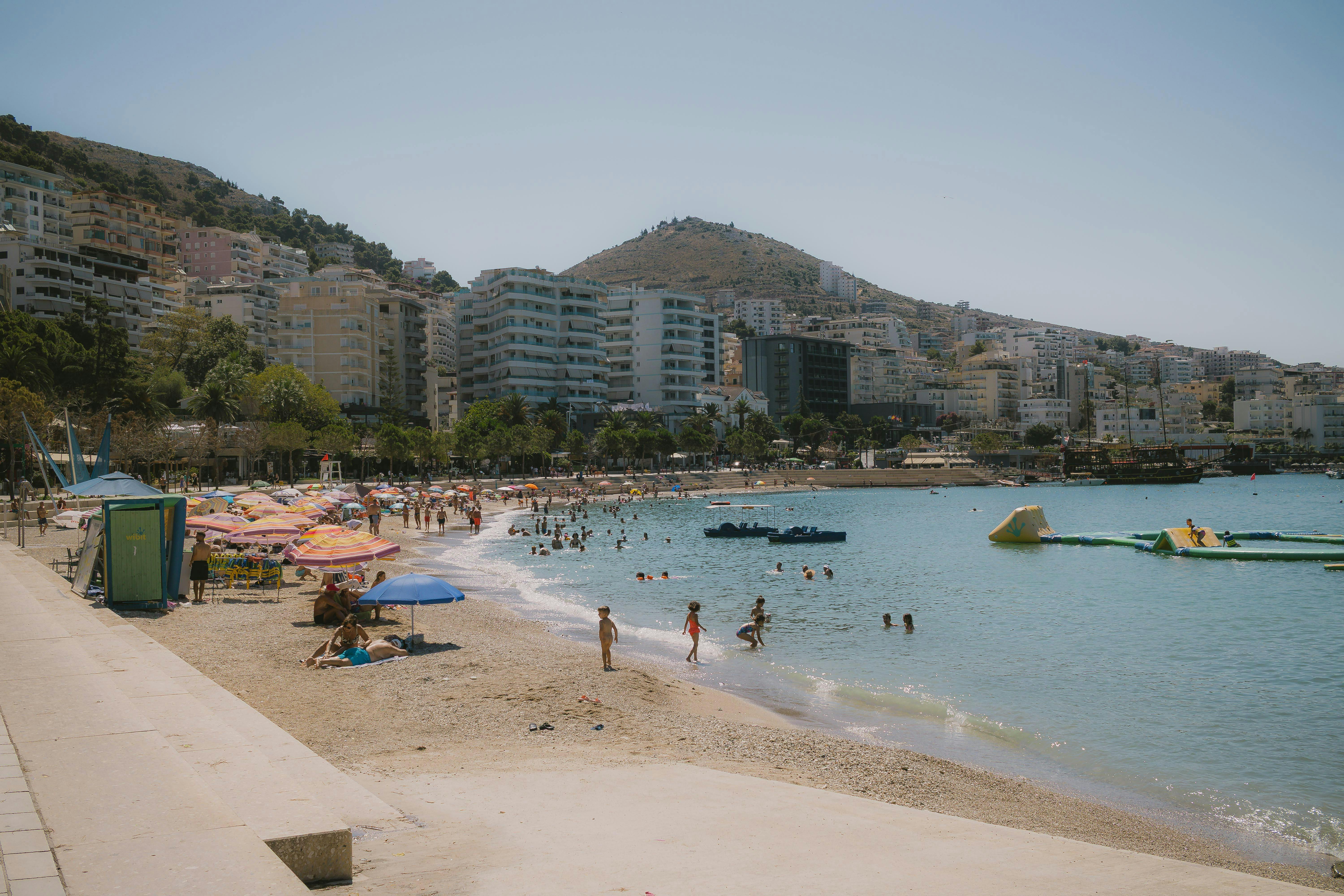 A vibrant day at the bustling beach in Sarandë, Albania, with people enjoying the sun and sea.