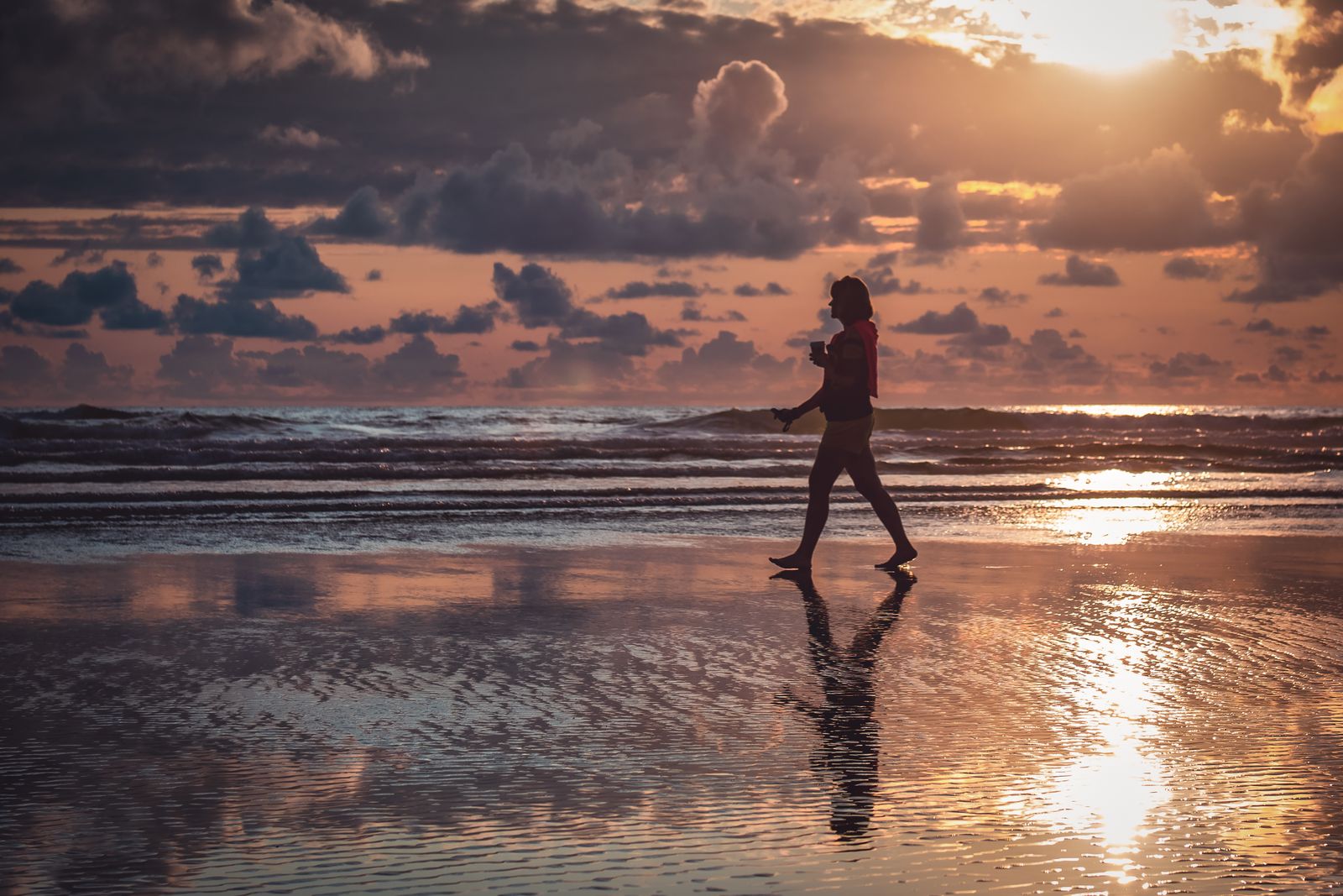 Woman walking along the shoreline at sunset