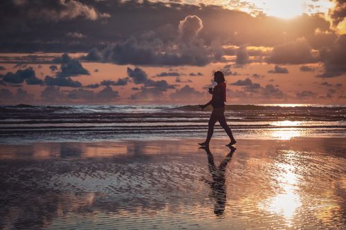 Free A woman walks along Cannon Beach, Oregon at sunset, reflecting in the wet sand. Stock Photo