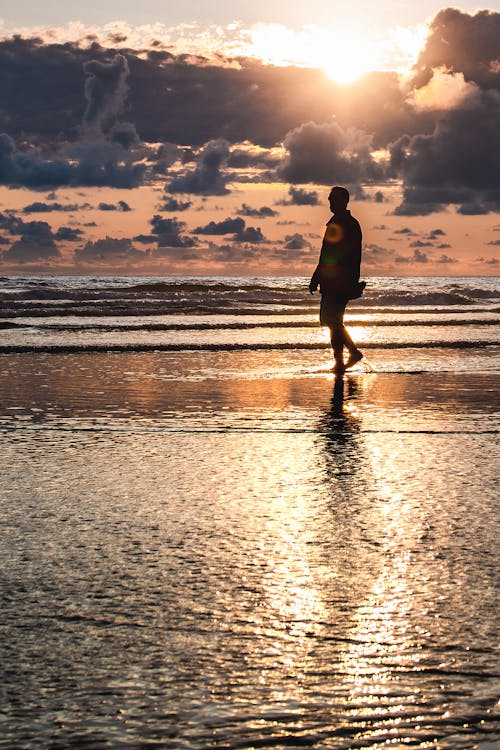 Man Walking on Seashore during Golden Hour