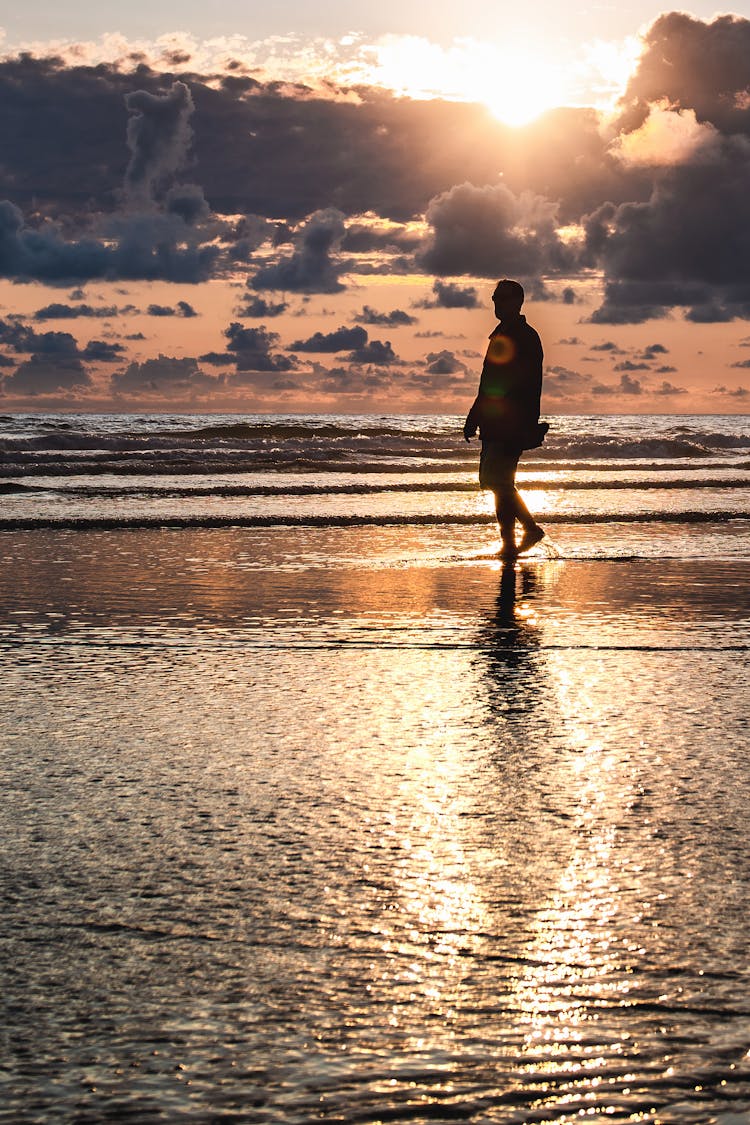 Man Walking On Seashore During Golden Hour