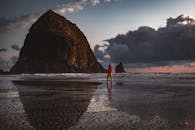 日落时分，一名女子在坎农海滩平静地散步，干草堆岩作为背景