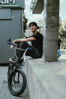A young man in casual attire relaxing with his BMX bike on a city street in Tbilisi, Georgia.