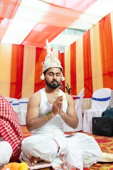 Cultural elegance at a Bengali wedding with a groom in traditional attire during a prayer ceremony.