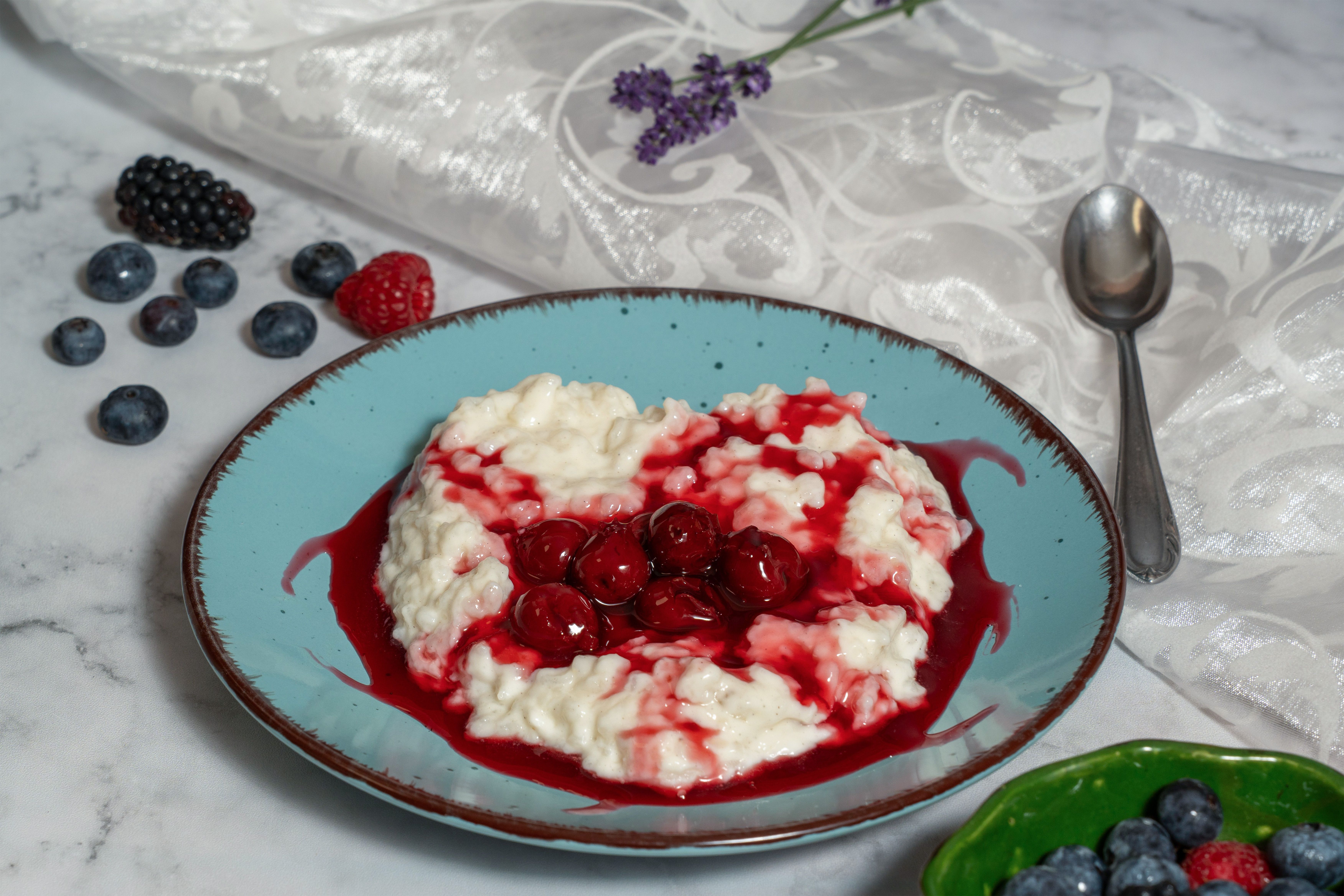 A vibrant plate of creamy rice porridge topped with fresh berries and red sauce, perfect for a sweet breakfast.