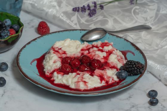 Mound of creamy rice pudding swirled with red cherry sauce on a turquoise plate with berries