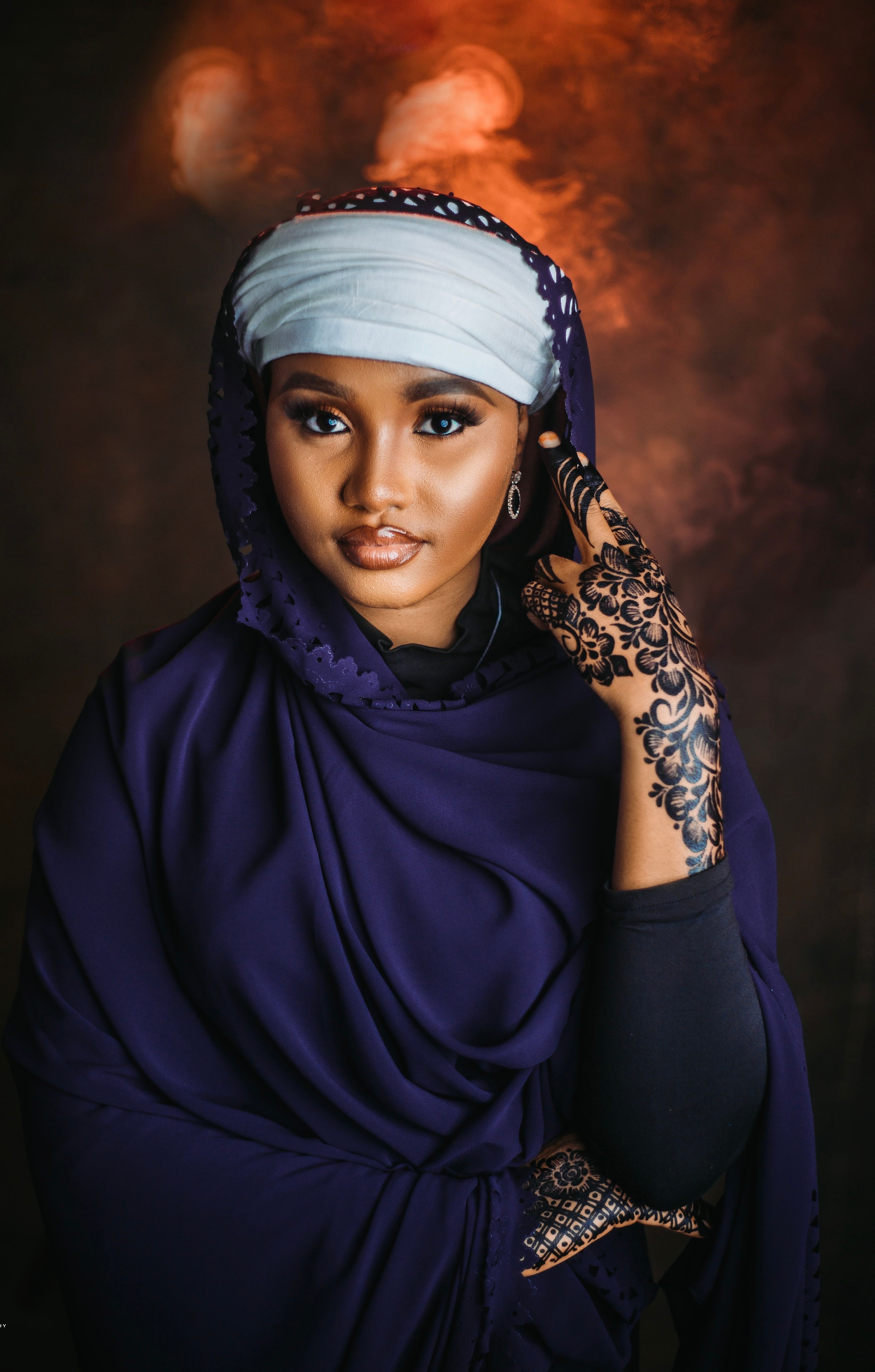 Portrait of a woman in a purple hijab with intricate henna design against a moody background.