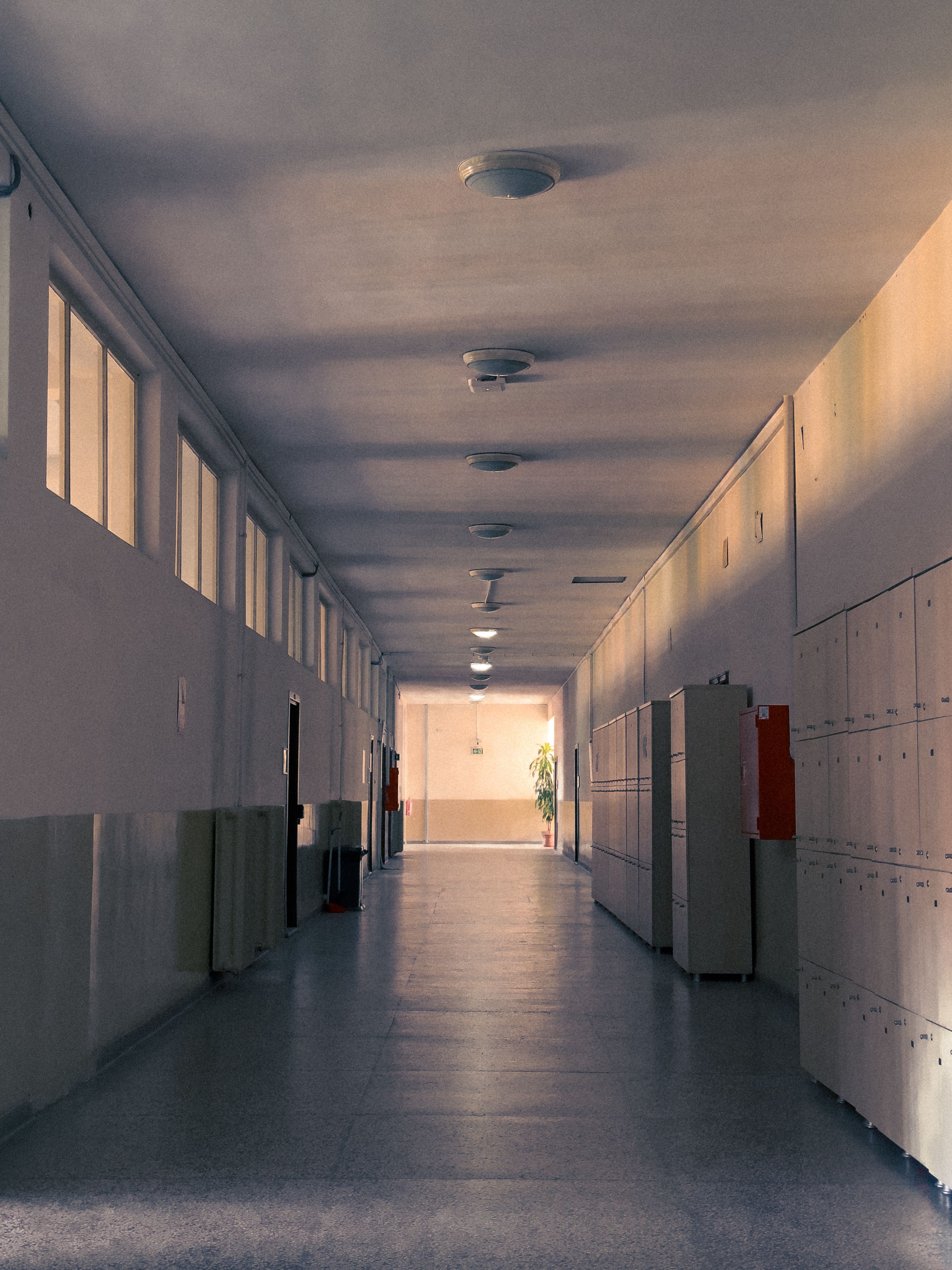 Long couloir d'établissement scolaire bordé de casiers, éclairé en enfilade