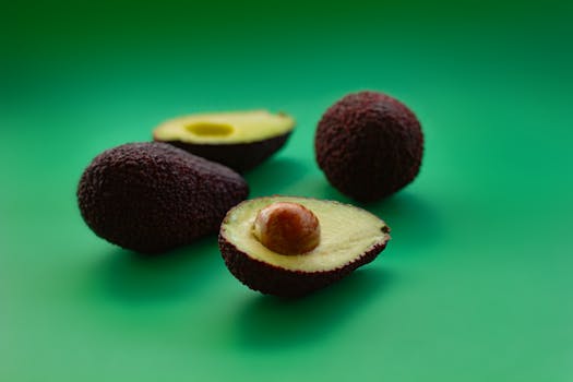 Three fresh avocados, including a halved one, on a vibrant green background, showcasing their textured skin.