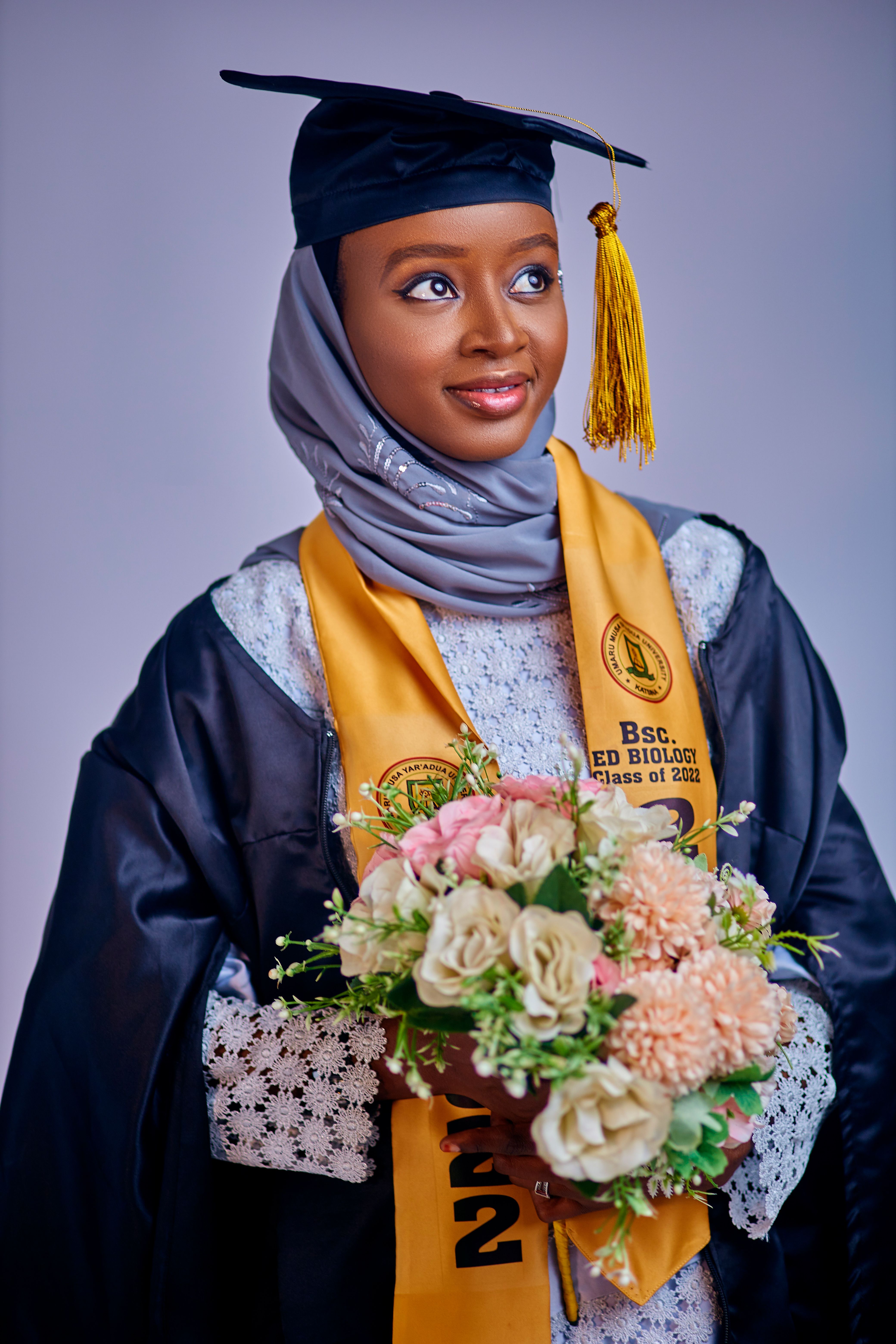 Smiling graduate in cap and gown holding a bouquet, celebrating academic achievement.