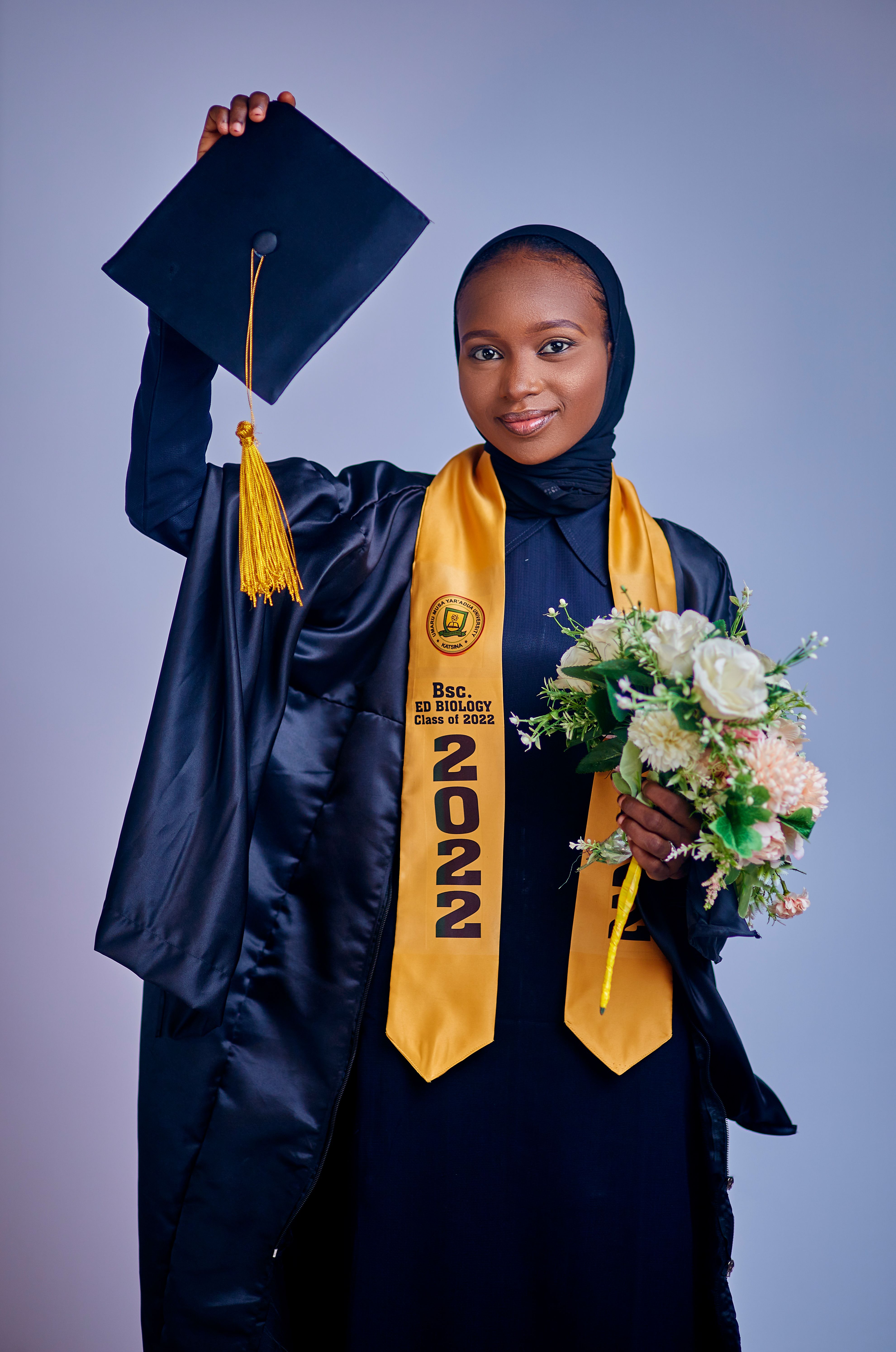 Young woman celebrating graduation in cap and gown with flowers.