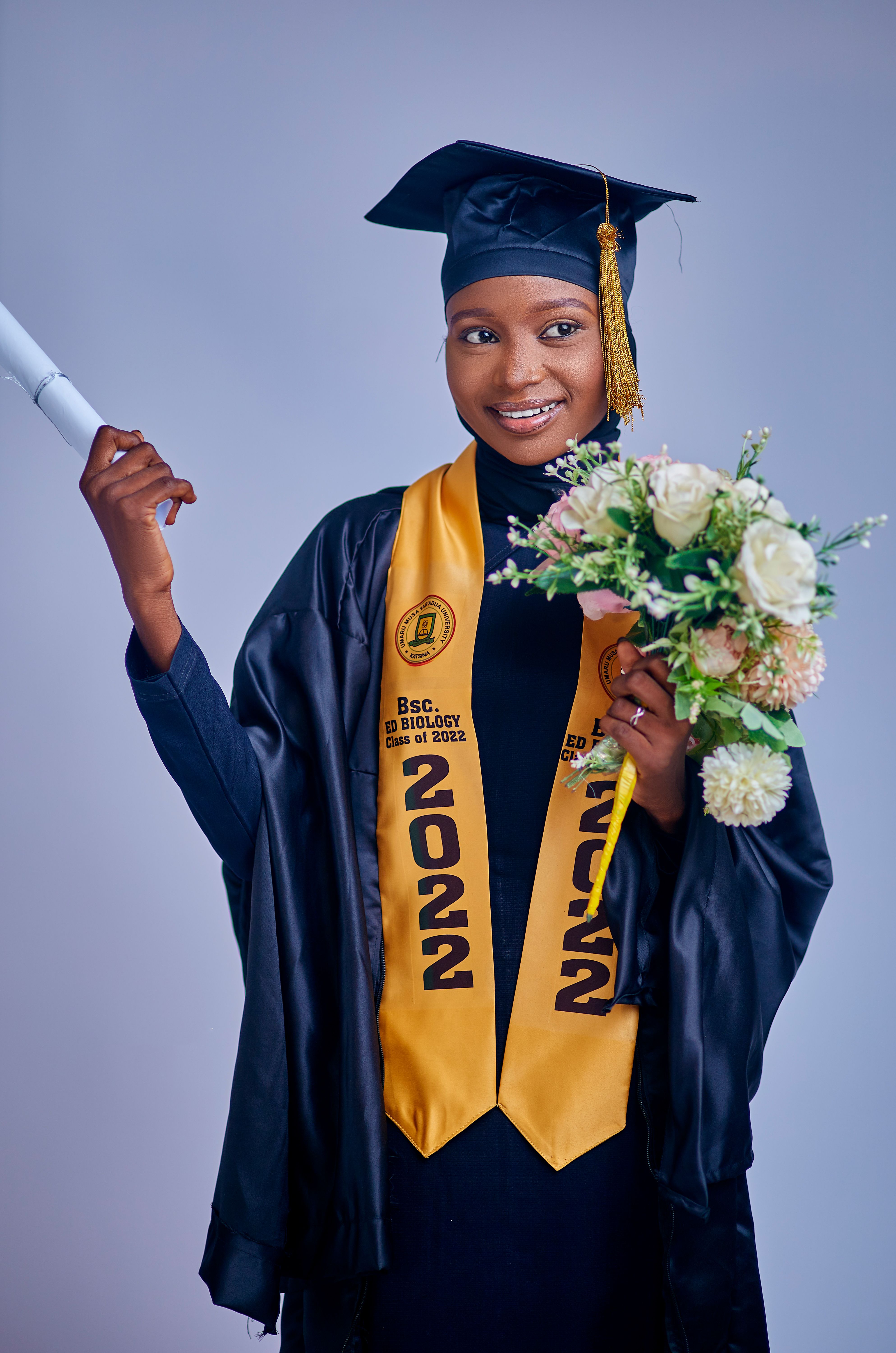 Proud graduate in cap and gown holding diploma and flowers, smiling.