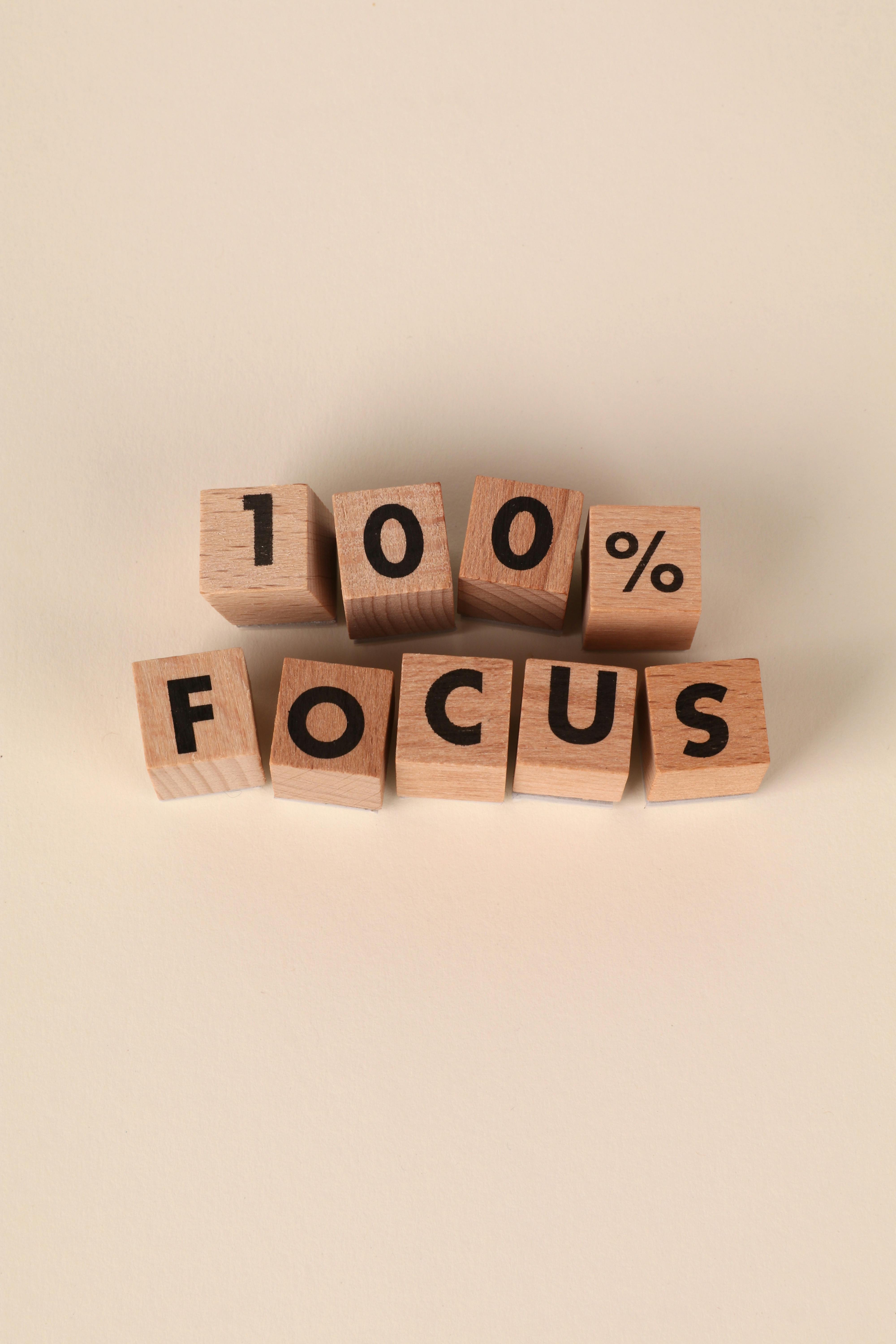 Wooden blocks spelling '100% FOCUS', symbolizing motivation and concentration.