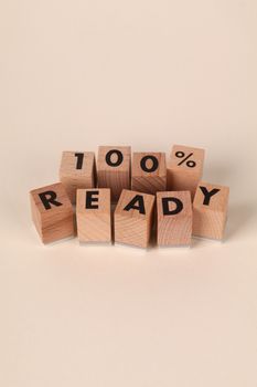 Wooden blocks spell out '100% Ready' on a neutral background, symbolizing preparation.