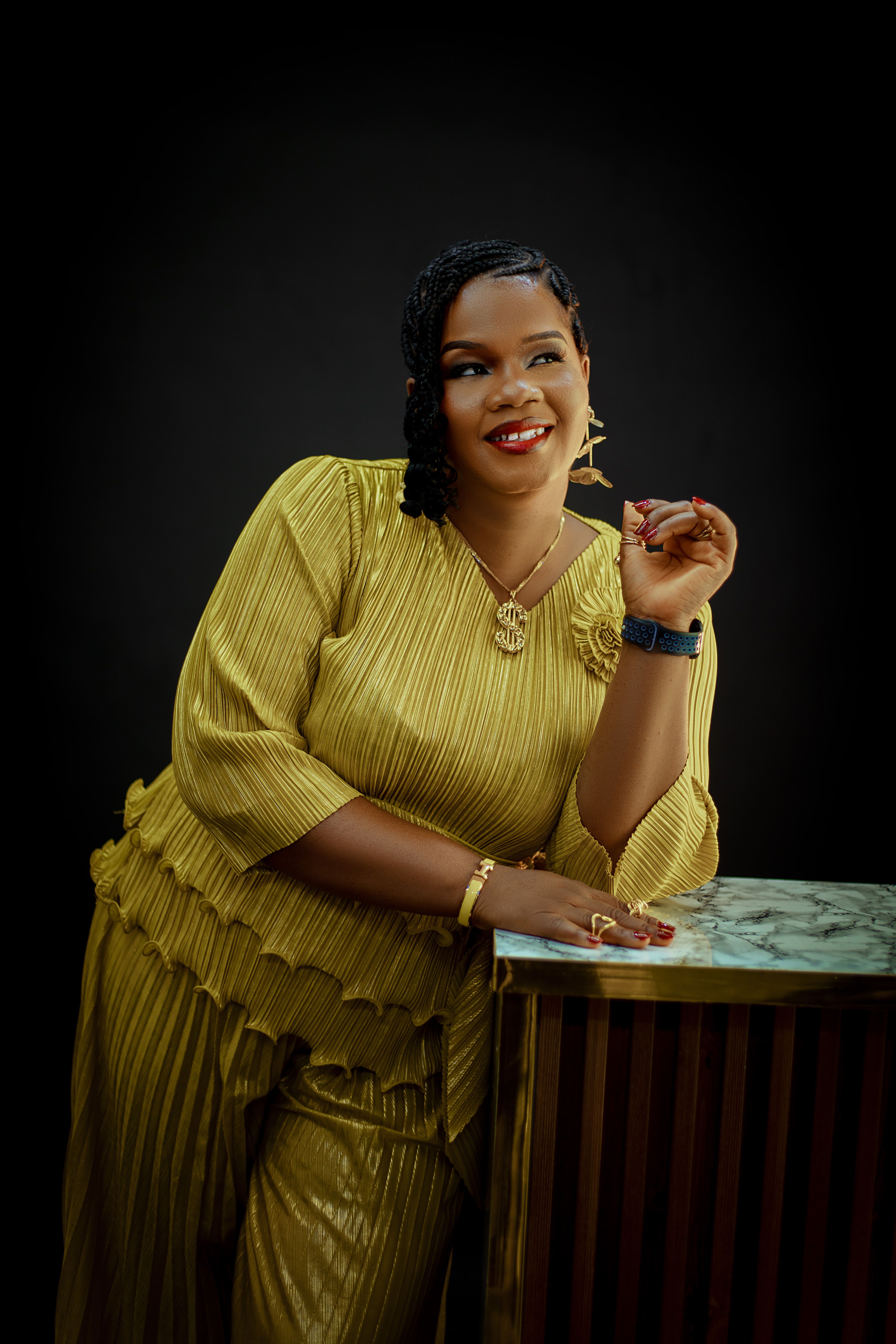 Stylish woman in gold dress poses elegantly against a dark background.