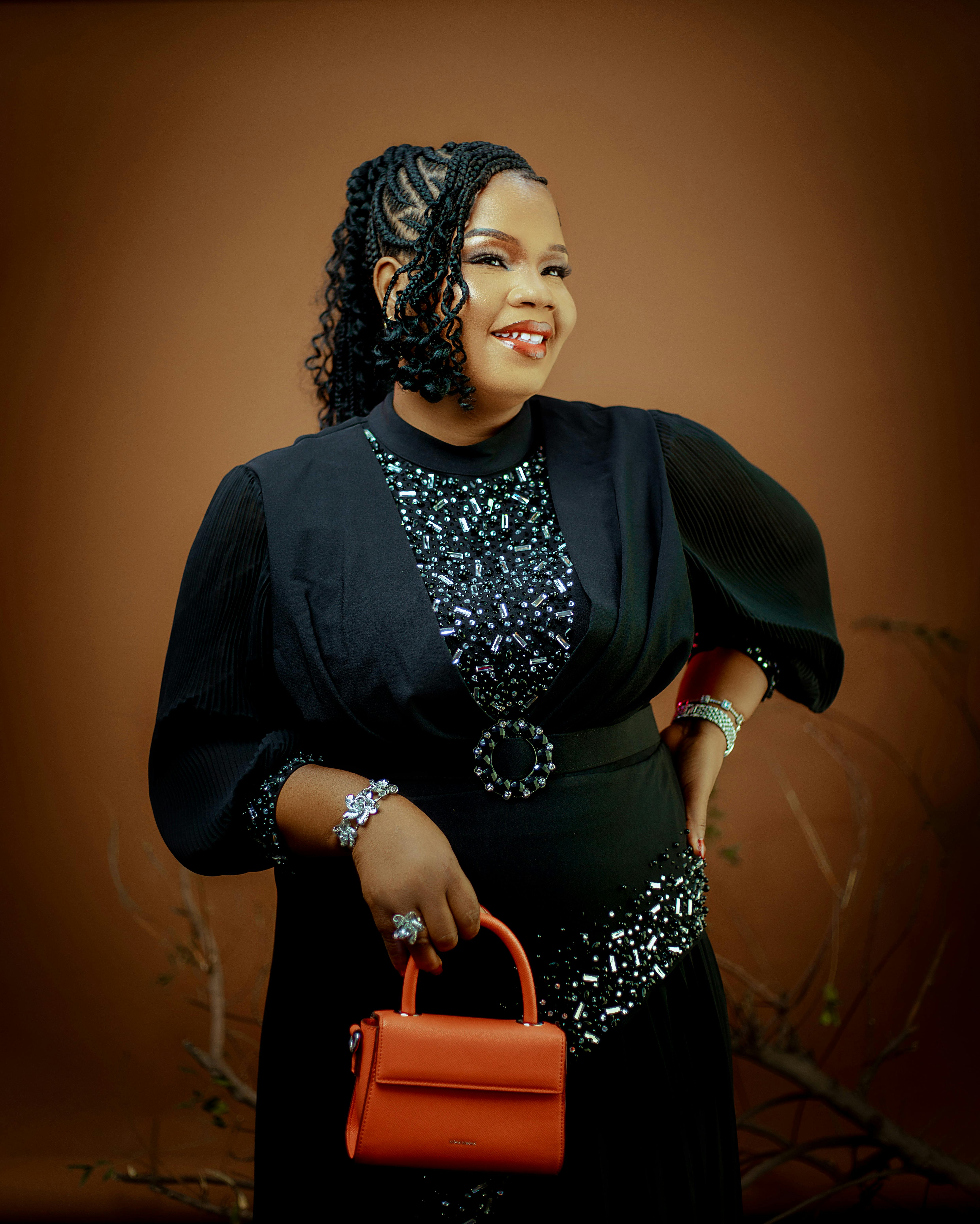 Stylish woman in a sparkling black dress with an orange handbag. Perfect for fashion themes.