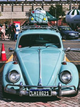 Vintage blue Volkswagen Beetle with model car on roof at outdoor auto show.