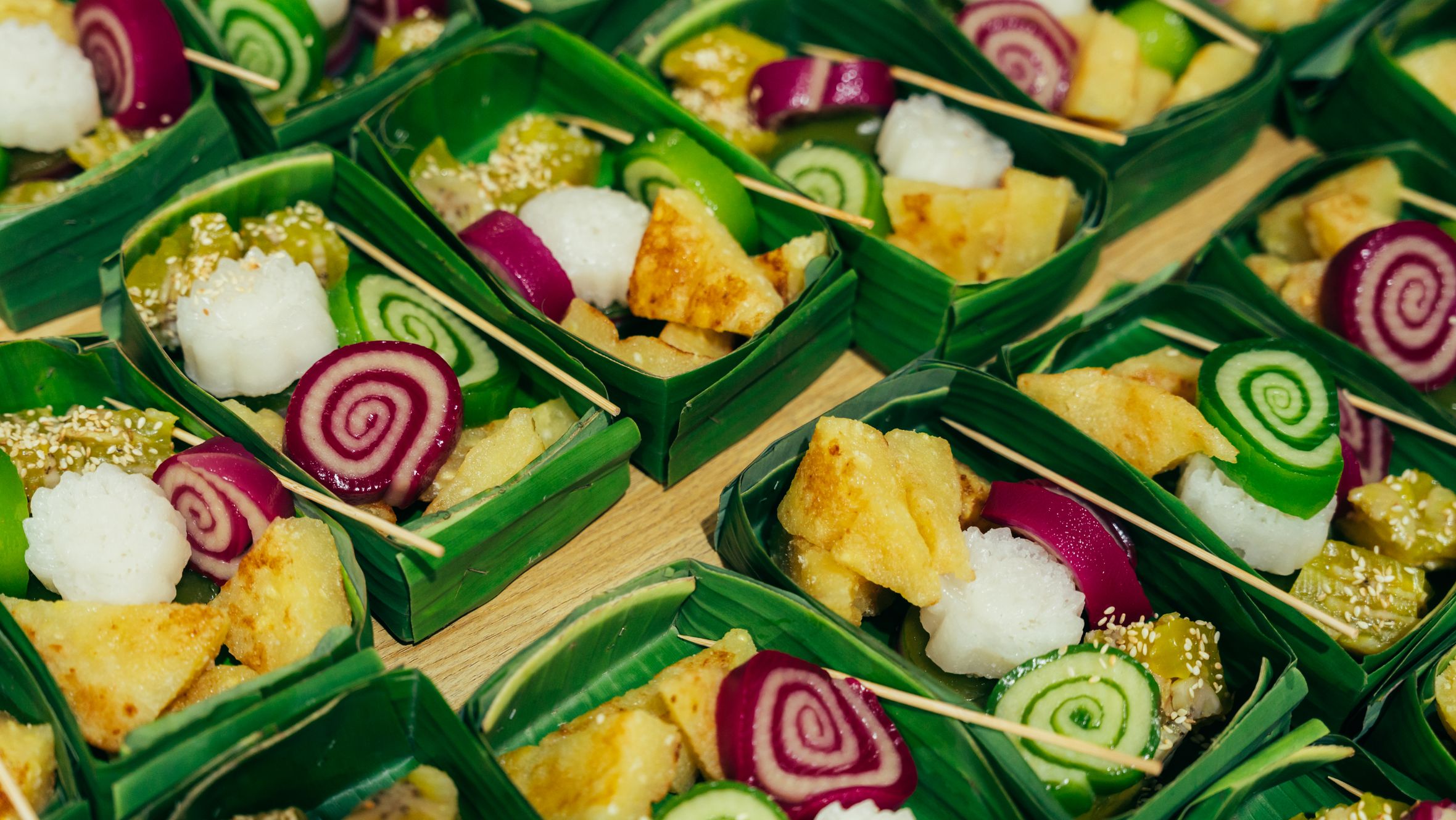 Colorful Vietnamese sweets presented in banana leaf trays, showcasing traditional dessert art.