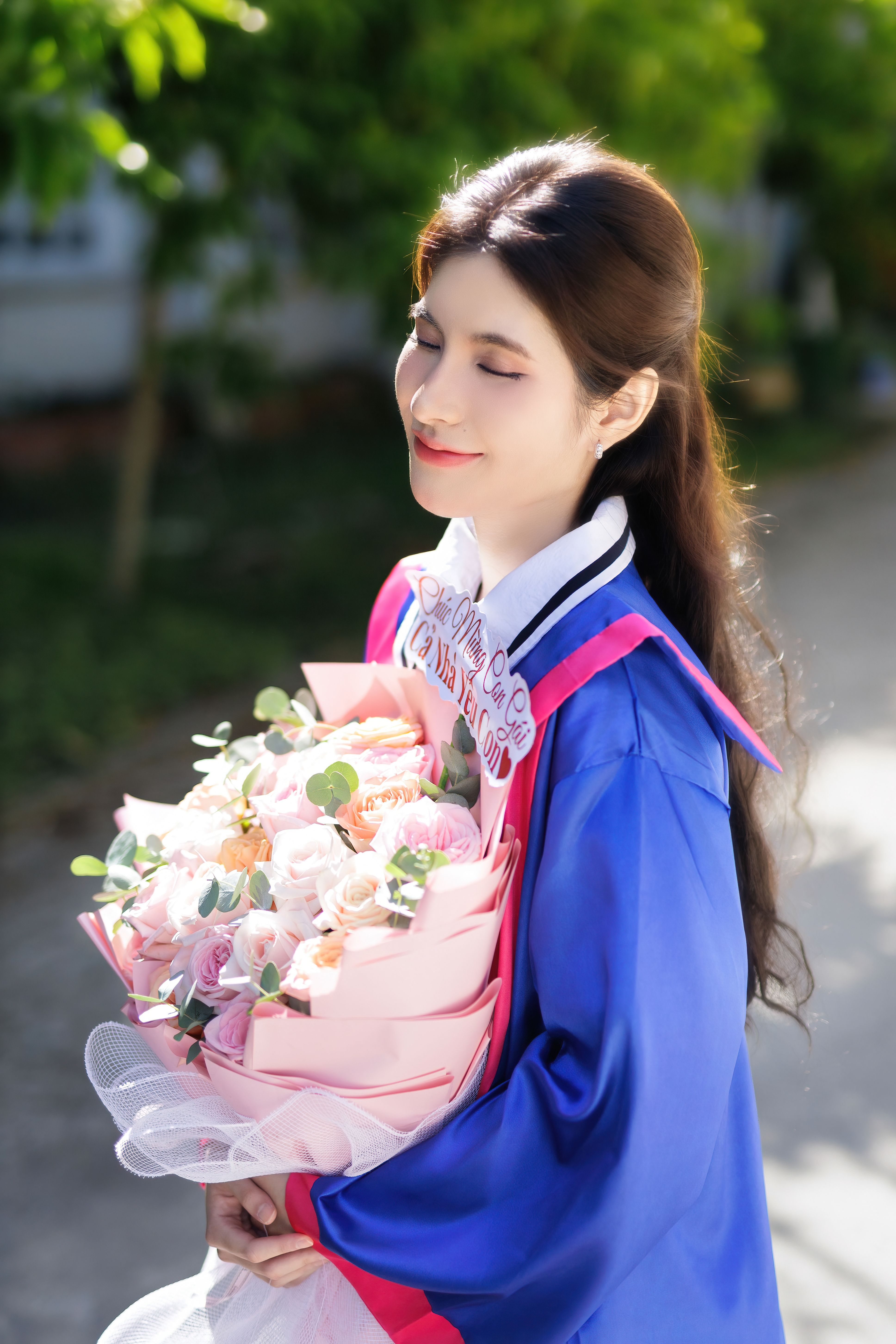 Graduate in Cap and Gown Holding Flowers Outdoors · Free Stock Photo